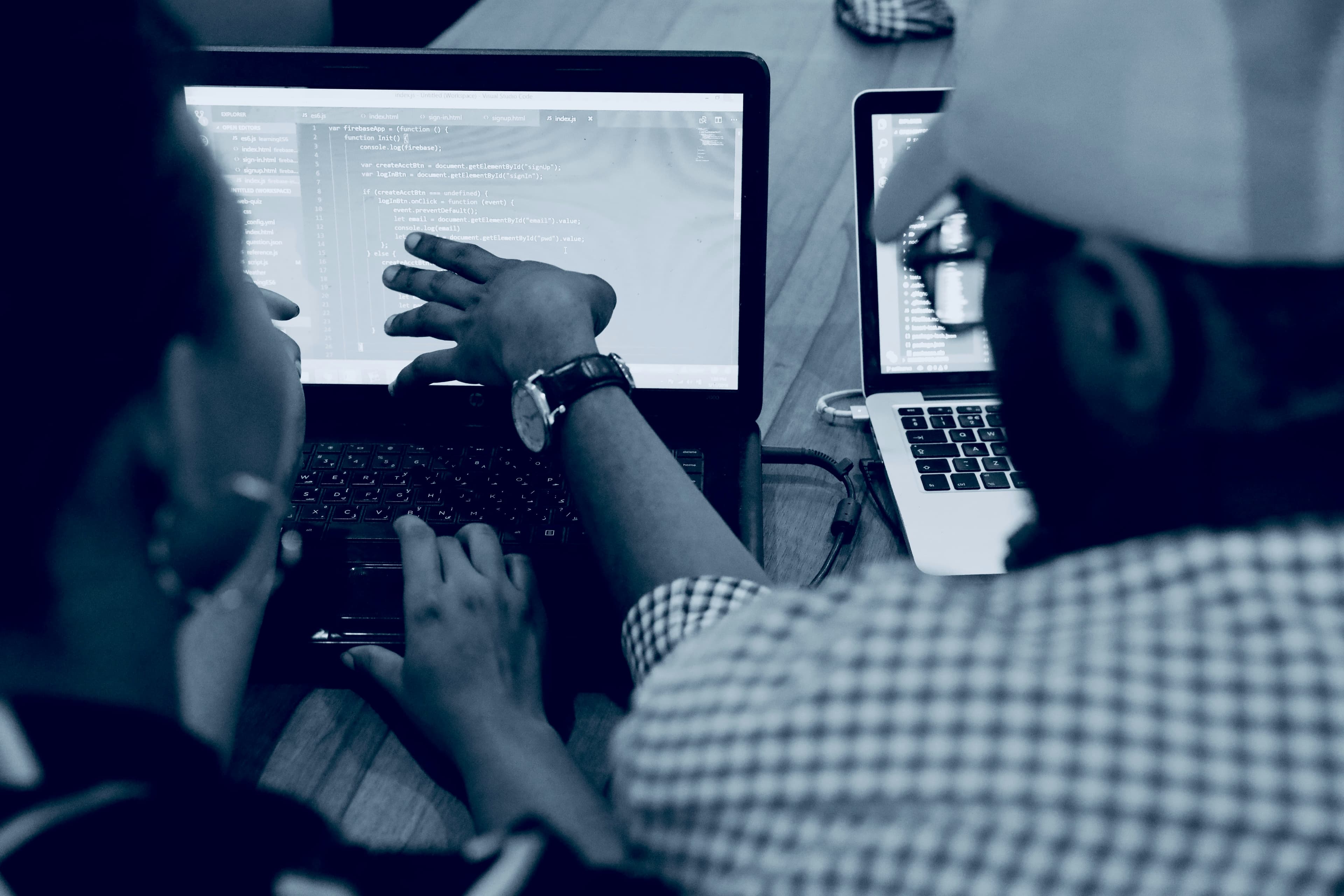 Image of a person giving coding guidance to another person on a laptop.
